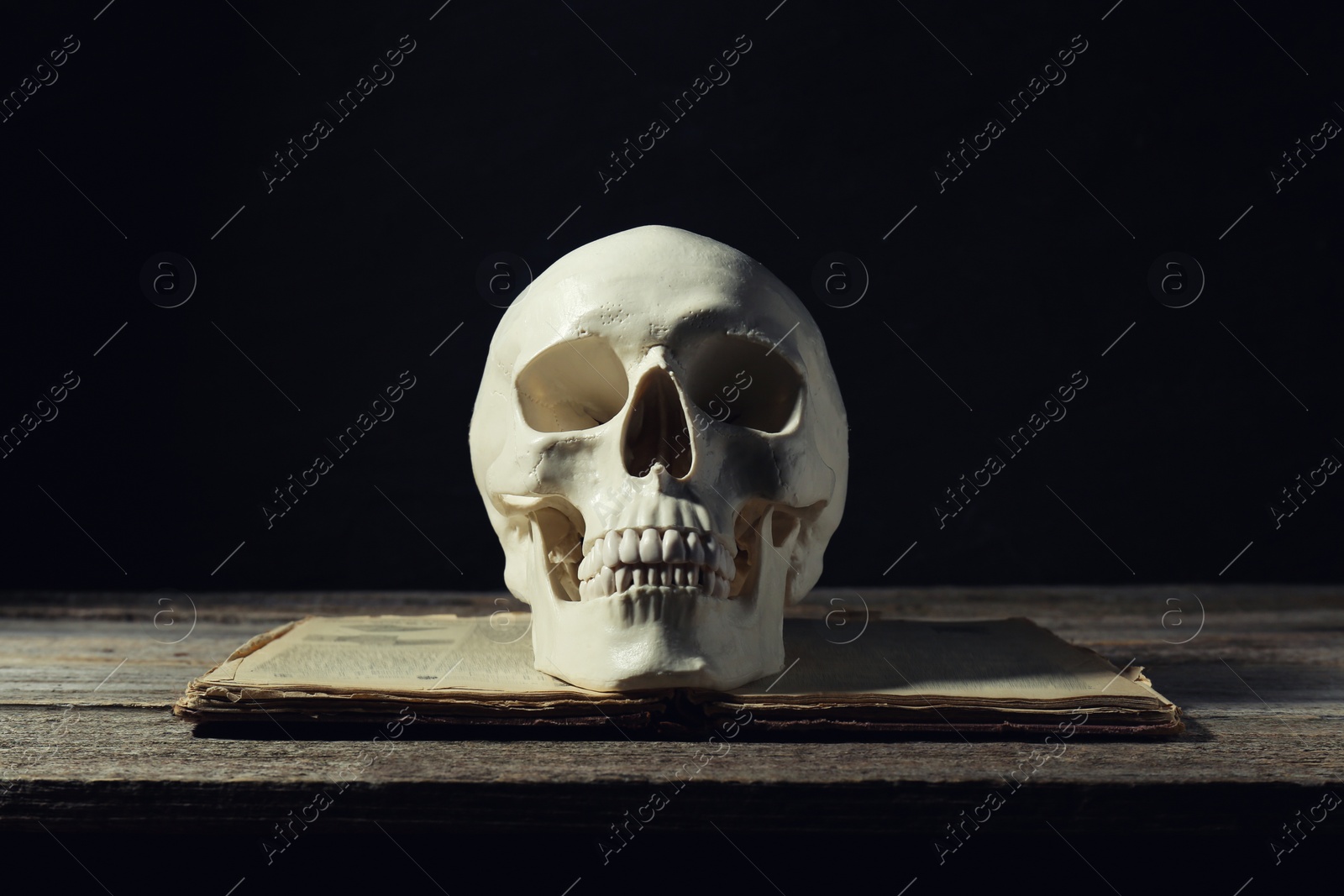 Photo of Human skull and old book on wooden table against black background