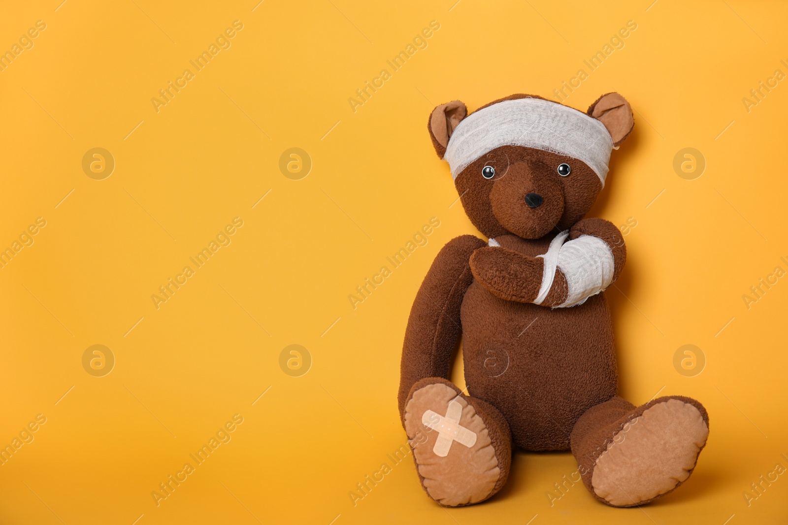 Photo of Toy bear with bandages on yellow background. Space for text