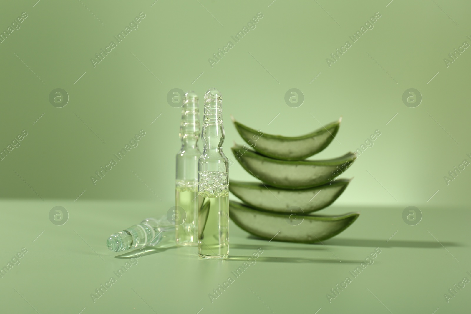 Photo of Skincare ampoules with extract of aloe vera and cut leaves on pale green background