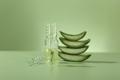 Skincare ampoules with extract of aloe vera and cut leaves on pale green background