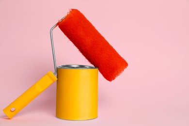 Can of orange paint and roller on pink background. Space for text