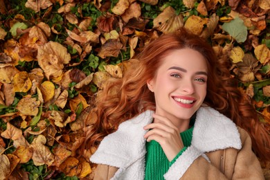 Photo of Smiling woman lying among autumn leaves outdoors, top view. Space for text