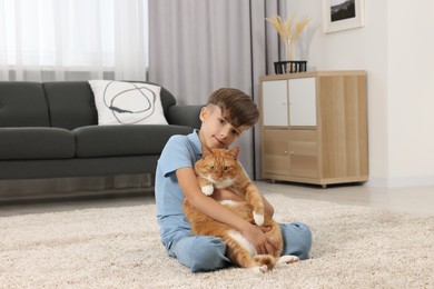 Photo of Little boy with cute ginger cat on soft carpet at home