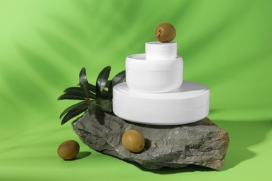 Photo of Jars of natural cream, stone and olives on light green background. Cosmetic products