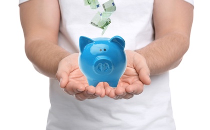 Young man and Euro banknotes falling into piggy bank on white background, closeup 