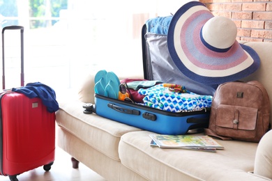 Photo of Open suitcase with different clothes and accessories on sofa indoors. Packing for vacation