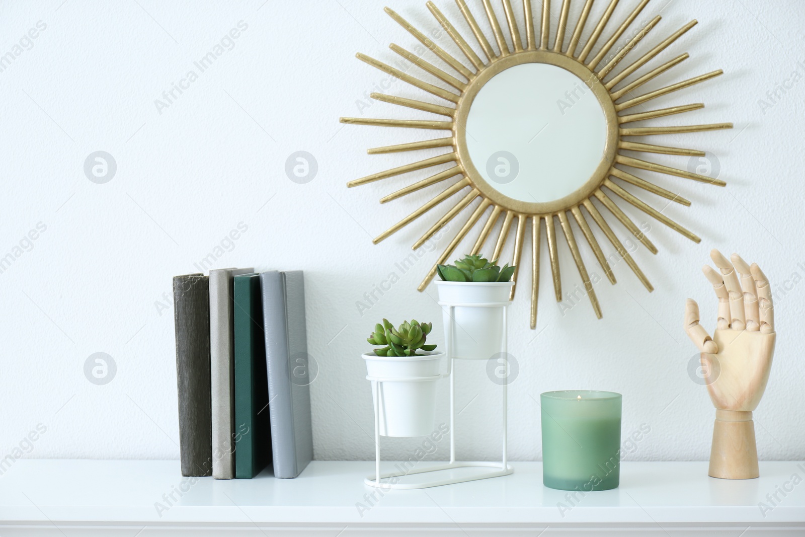 Photo of Burning candle, books and plants on shelf indoors. Interior elements