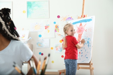 Photo of Cute little child painting on easel at lesson indoors