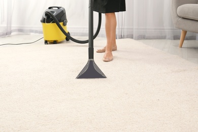 Photo of Woman removing dirt from carpet with vacuum cleaner indoors, closeup. Space for text