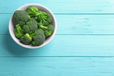 Bowl of fresh green broccoli on blue wooden table, top view. Space for text