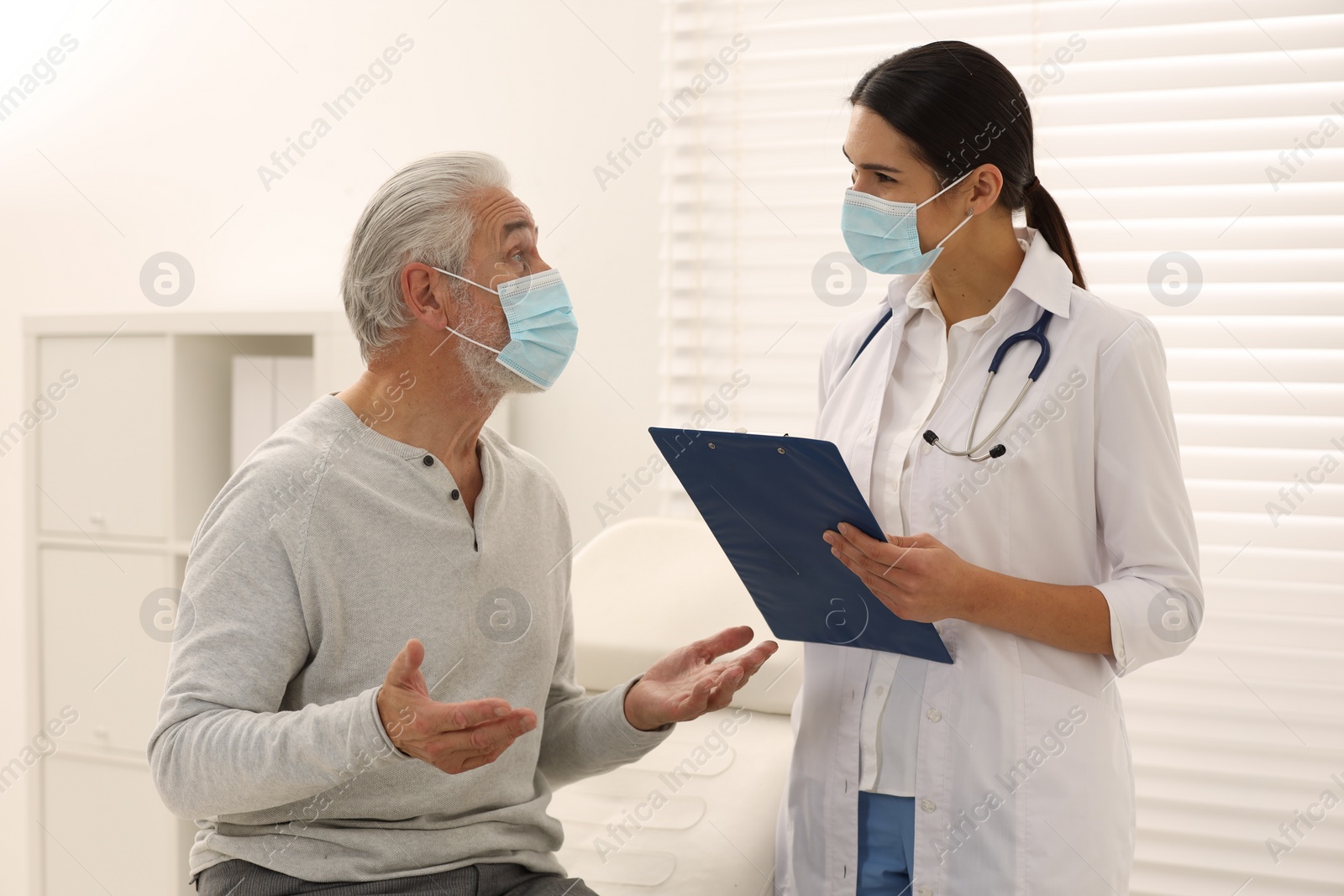 Photo of Nurse with clipboard talking to elderly patient in hospital