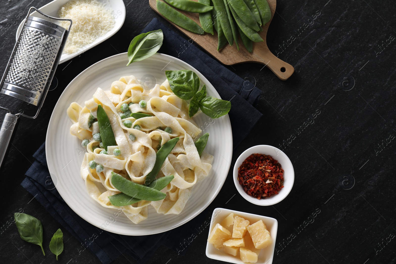 Photo of Delicious pasta with green peas and ingredients on black table, flat lay