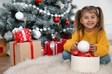 Photo of Cute little girl with box of Christmas balls at home