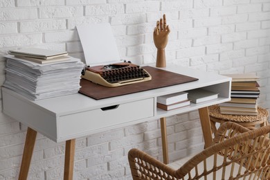 Photo of Comfortable writer's workplace with typewriter on desk near white brick wall