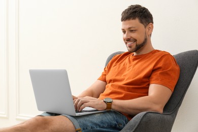 Photo of Happy man using laptop in armchair indoors. Internet shopping