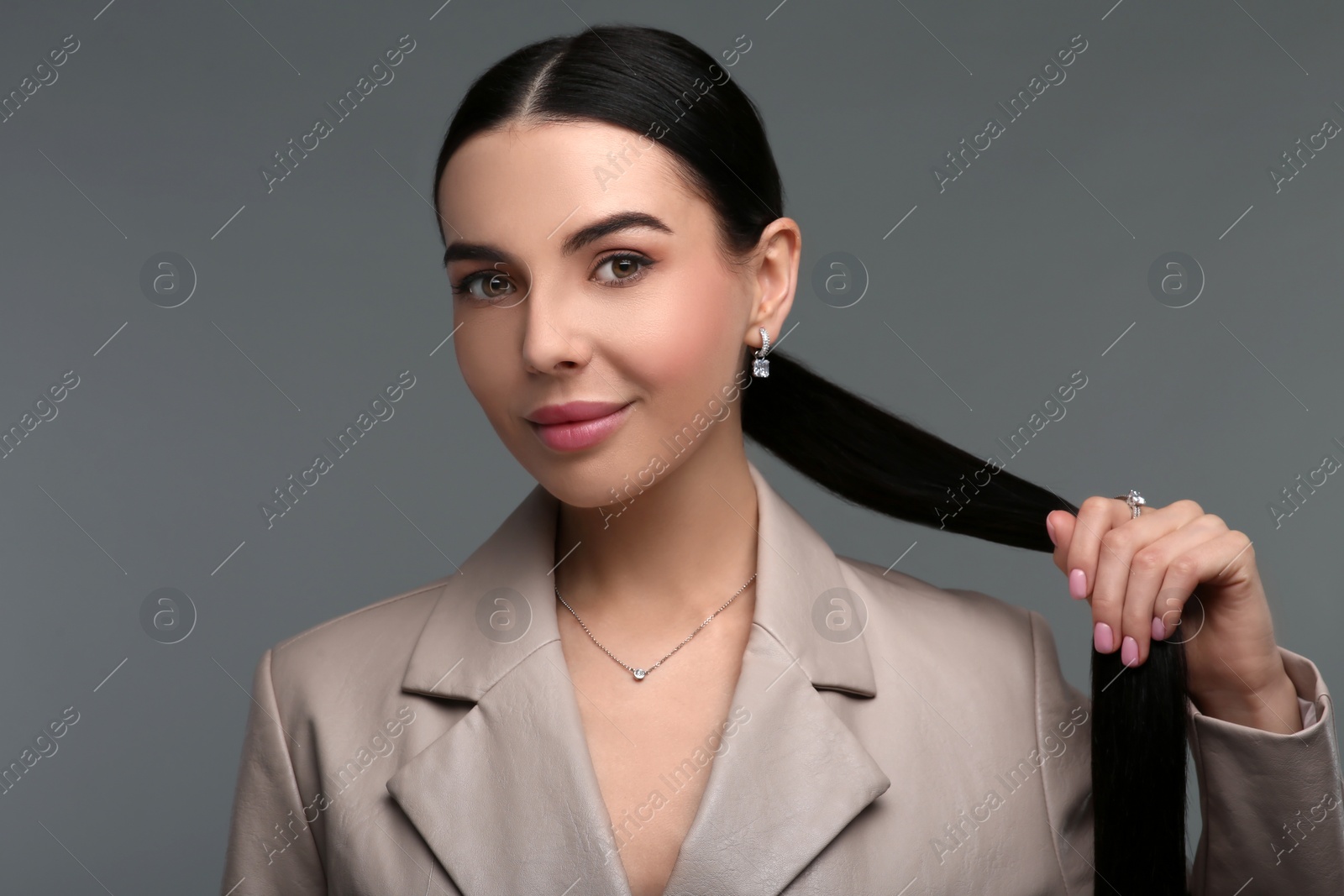 Photo of Beautiful young woman with elegant jewelry on dark grey background