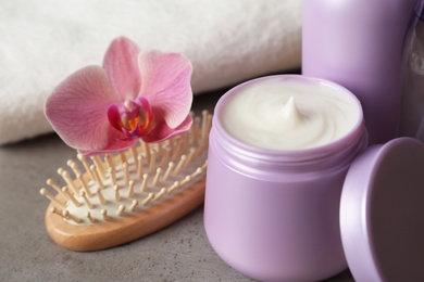 Different hair products, flower and brush on grey table, closeup