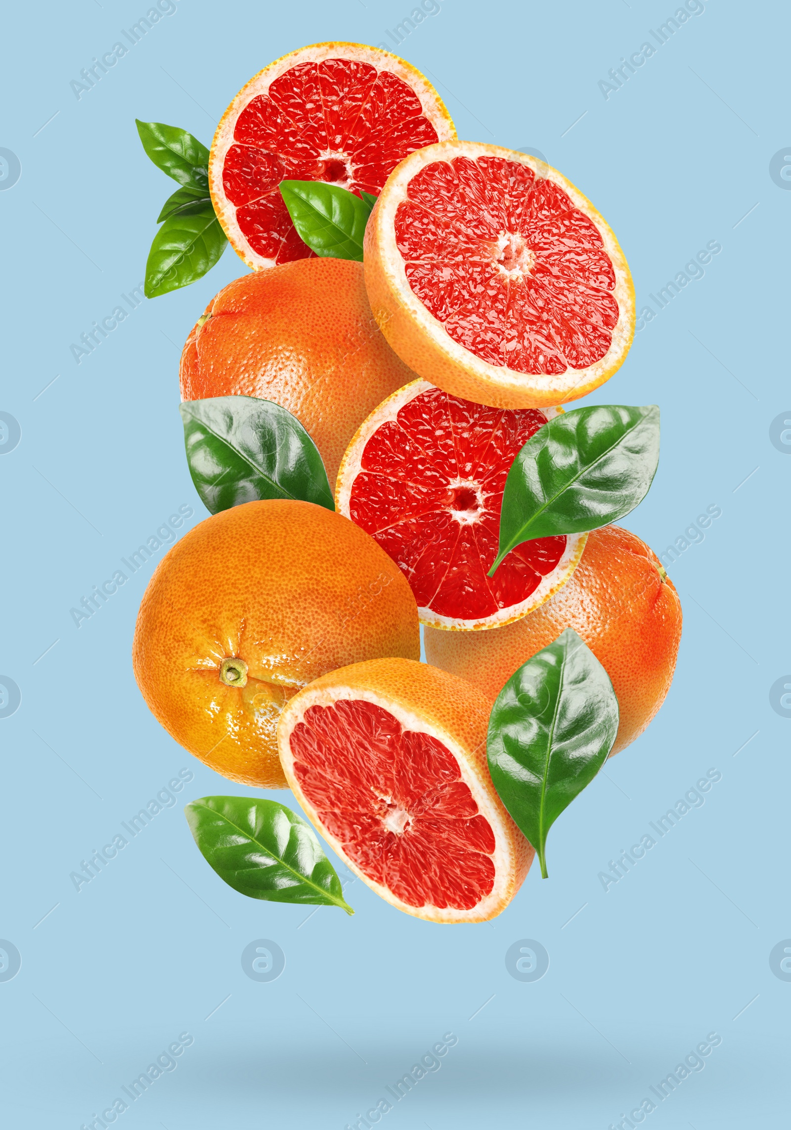 Image of Tasty ripe grapefruits and green leaves falling on light blue background