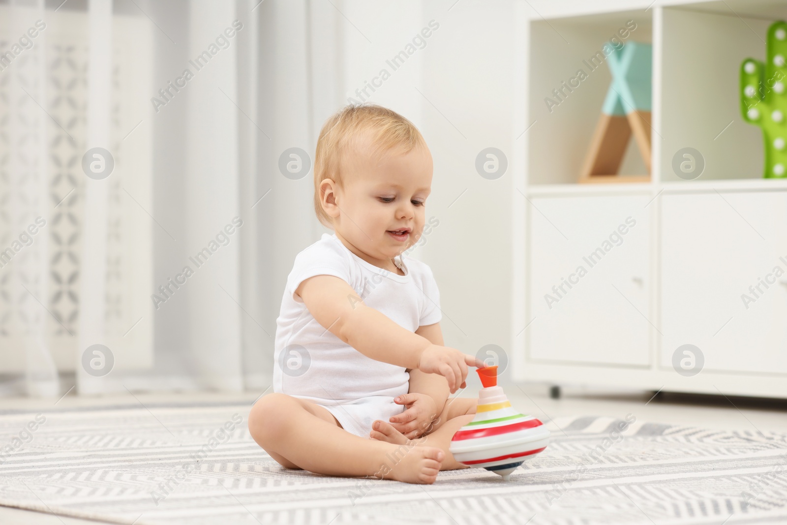 Photo of Children toys. Cute little boy playing with spinning top on rug at home