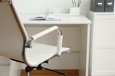 Modern office chair near table indoors, closeup. Stylish workplace interior