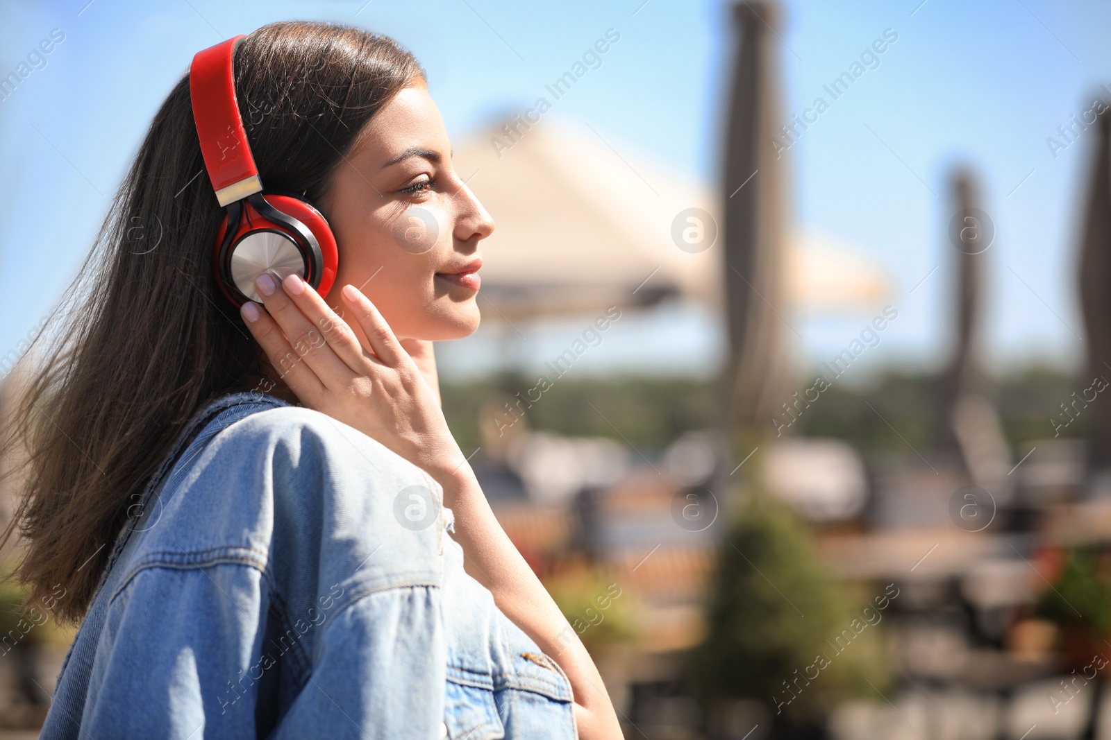 Photo of Young woman with headphones listening to music outdoors. Space for text