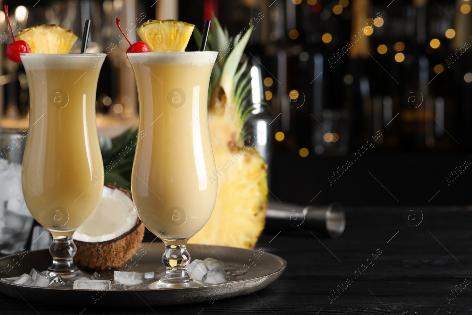 Photo of Tasty Pina Colada cocktails and ingredients on black wooden bar countertop, space for text