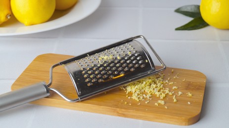 Photo of Wooden board with grater and fresh lemon zest on white tiled table
