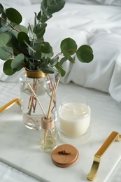 Photo of Eucalyptus branches, candle and aromatic reed air freshener on bed indoors, closeup. Interior elements