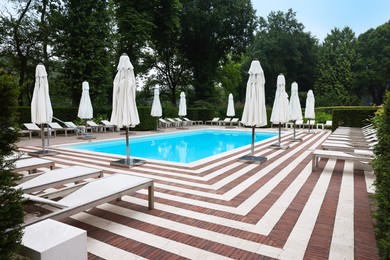 Photo of Many sunbeds and umbrellas near outdoor swimming pool