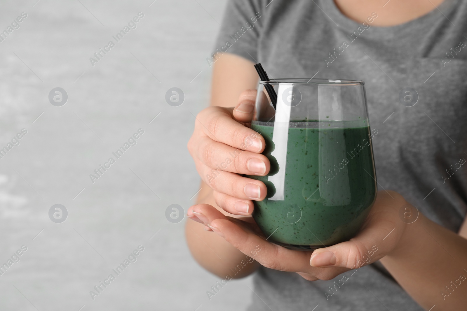 Photo of Woman holding glass of spirulina smoothie on grey background, closeup. Space for text