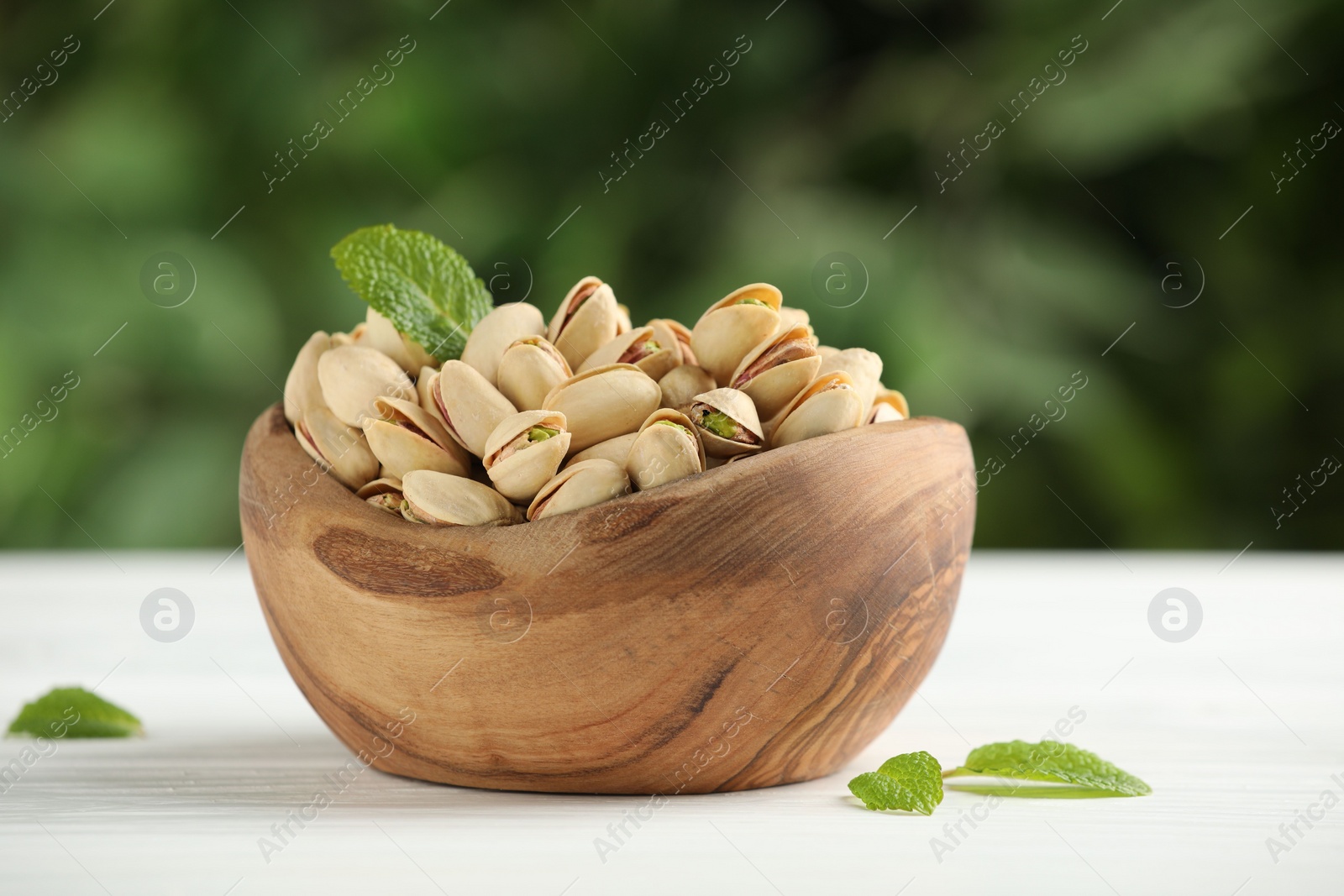 Photo of Tasty pistachios in bowl on white table against blurred background