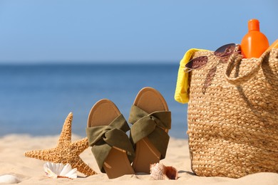 Bag with beach accessories and slippers on sand near sea