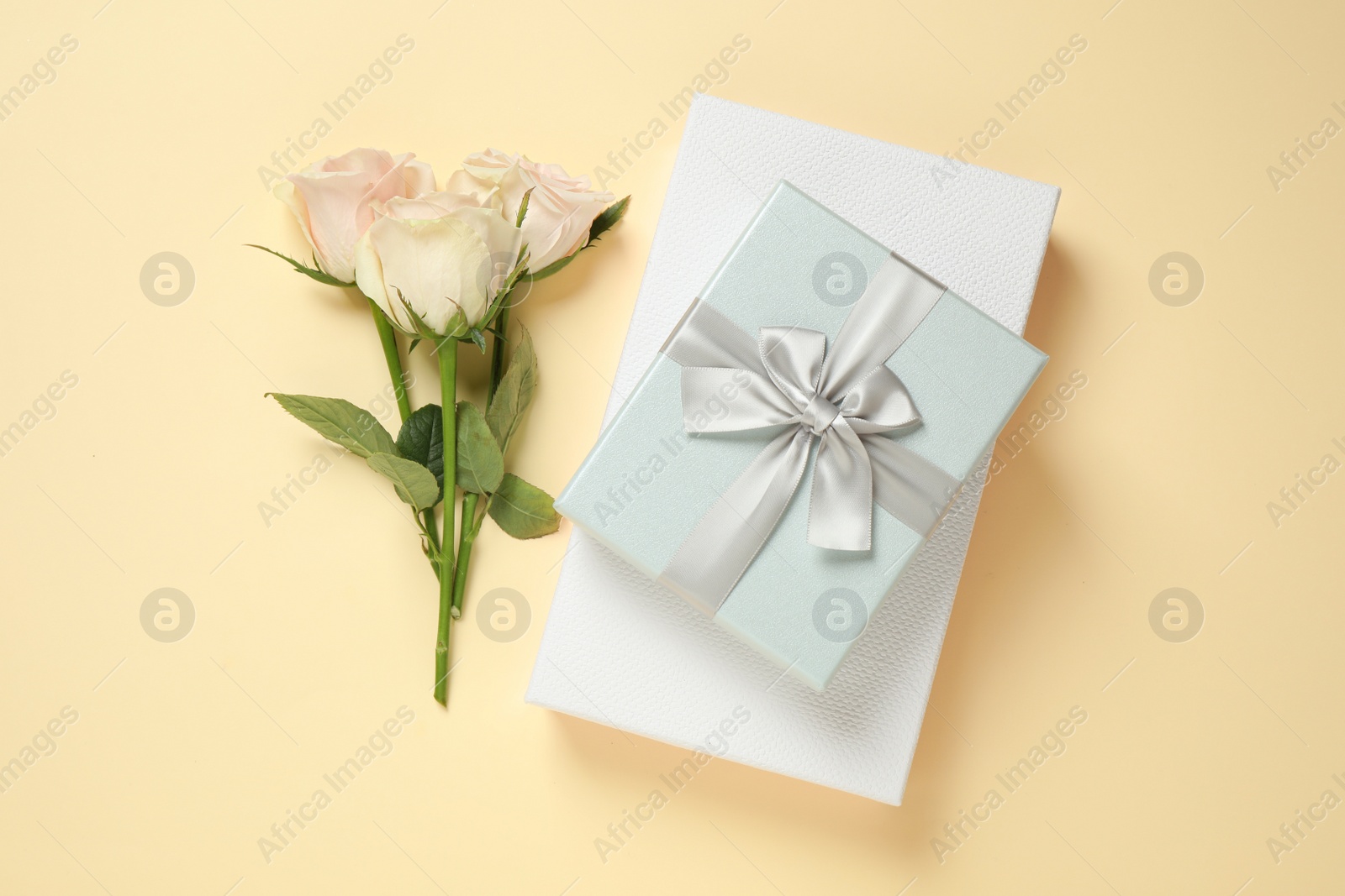 Photo of Elegant gift boxes and beautiful flowers on beige background, flat lay
