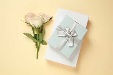 Photo of Elegant gift boxes and beautiful flowers on beige background, flat lay
