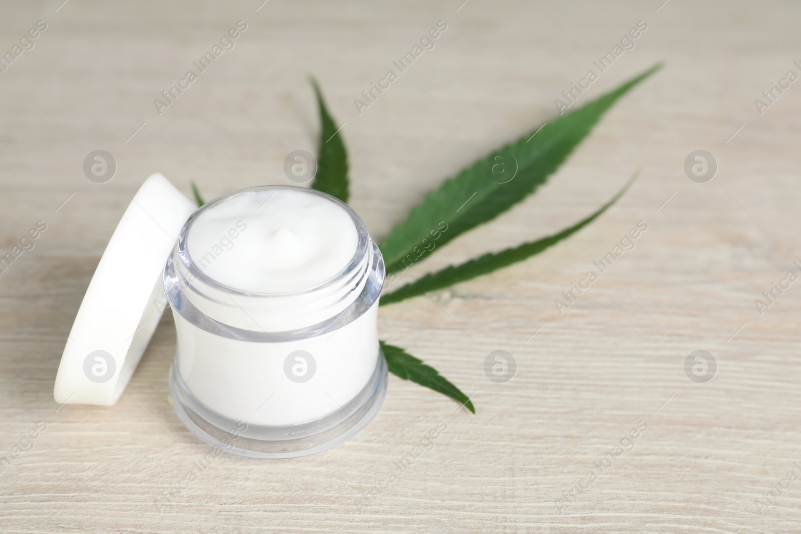 Photo of Glass jar of hemp cream and green leaf on wooden table, space for text. Natural cosmetics