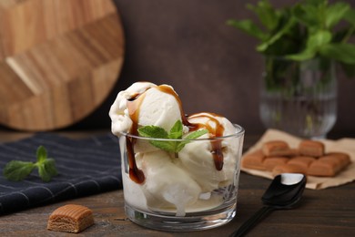 Photo of Scoopsice cream with caramel sauce, mint leaves and candies on wooden table, closeup