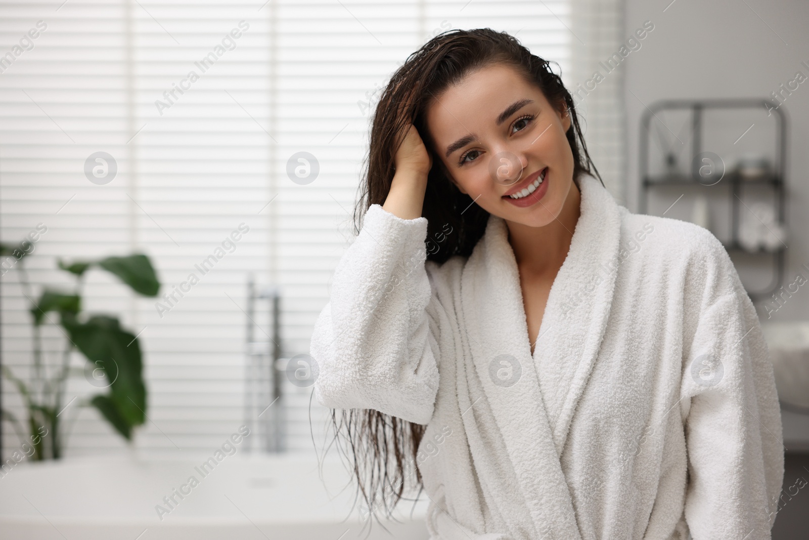 Photo of Smiling woman wearing bathrobe after shower in bathroom. Space for text