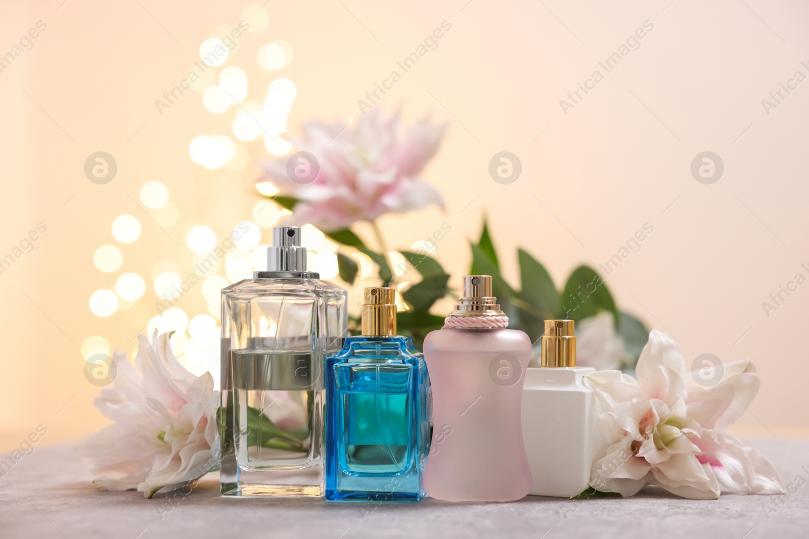 Photo of Perfume bottles and bouquet of beautiful lily flowers on table against beige background with blurred lights, closeup