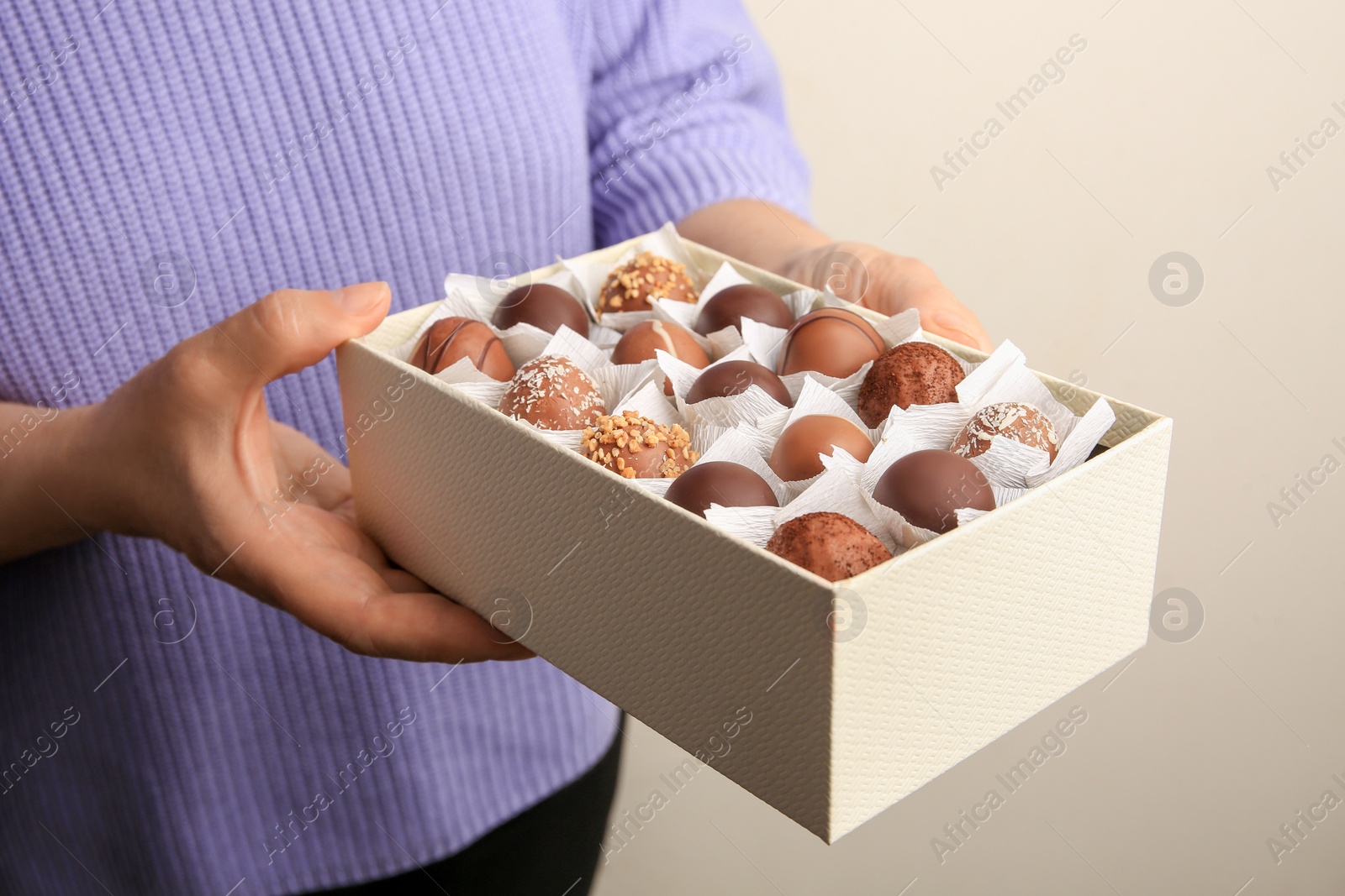 Photo of Woman holding box of delicious chocolate candies on light gray background, closeup