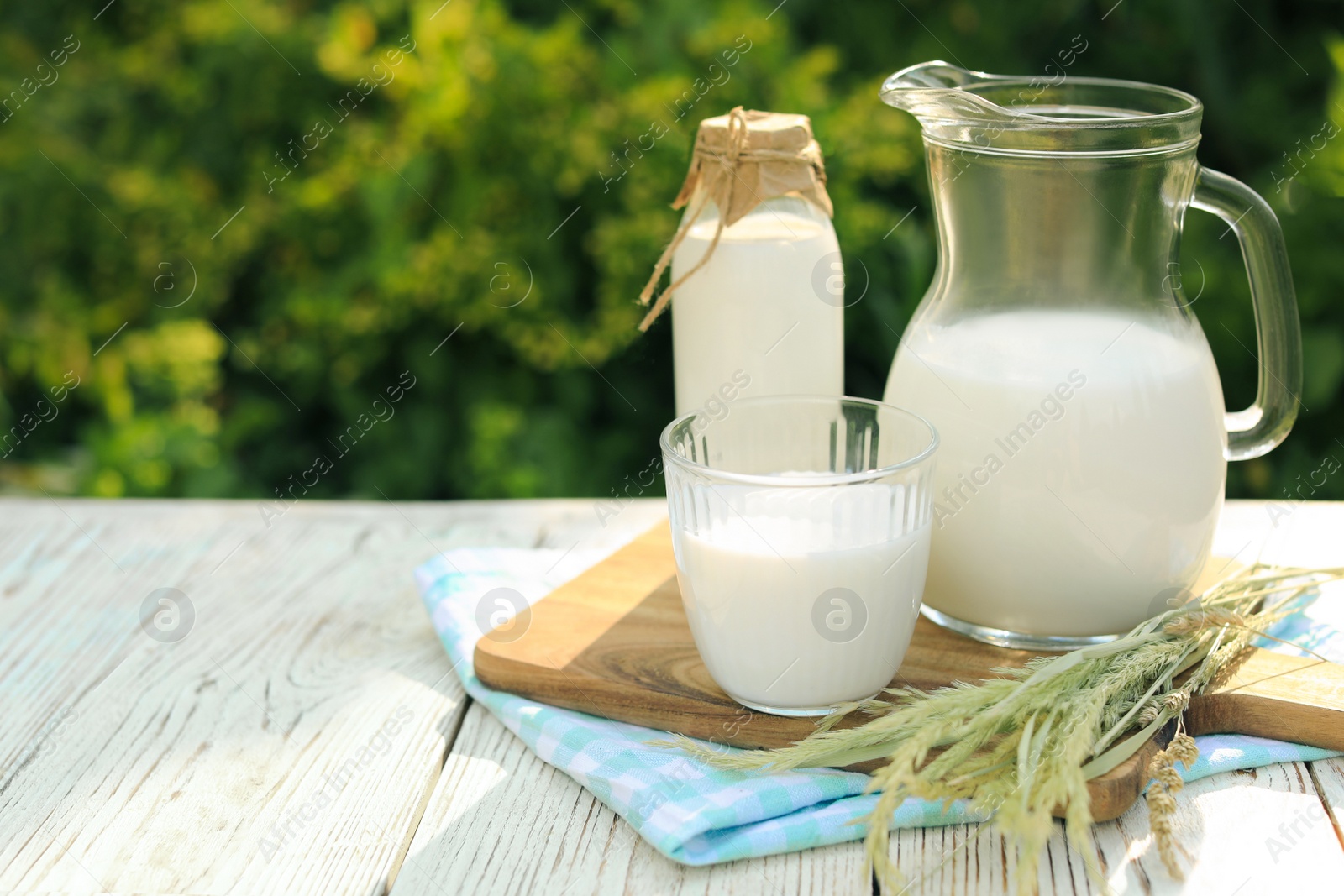 Photo of Jug, bottle and glass of tasty fresh milk on white wooden table outdoors, space for text
