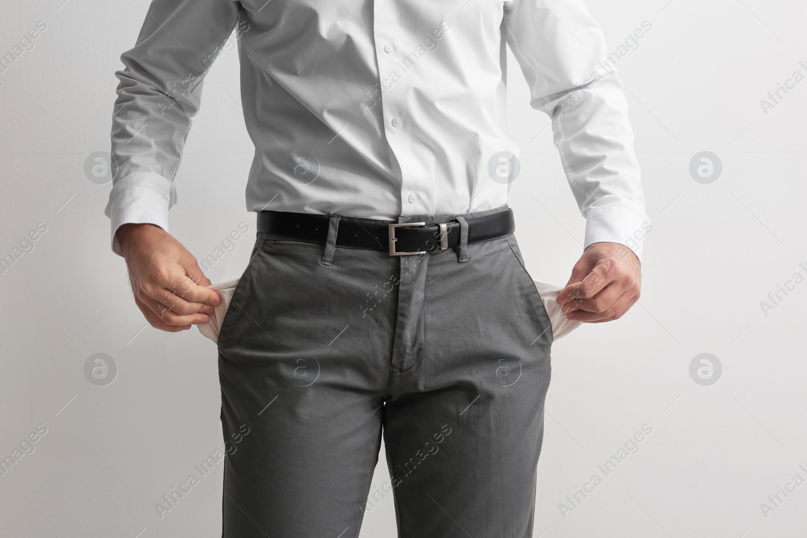 Photo of Businessman showing empty pockets on light background, closeup