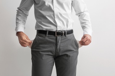 Businessman showing empty pockets on light background, closeup