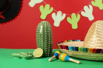 Composition with Mexican sombrero hat and maracas on green table, closeup