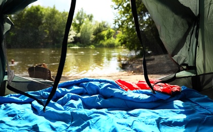 Camping tent with sleeping bag near lake, view from inside