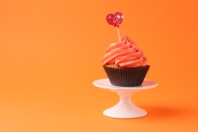 Photo of Delicious cupcake with bright cream and heart topper on orange background. Space for text