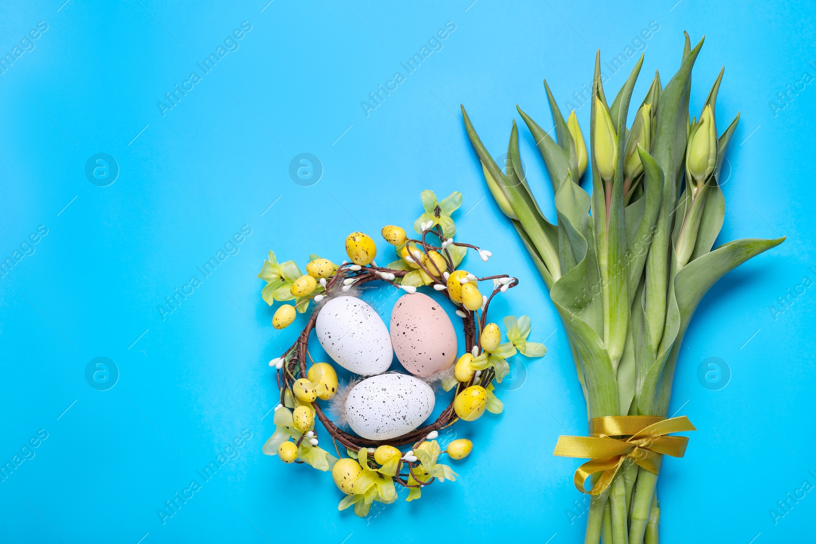 Photo of Flat lay composition with flowers and eggs on light blue background, space for text. Easter celebration