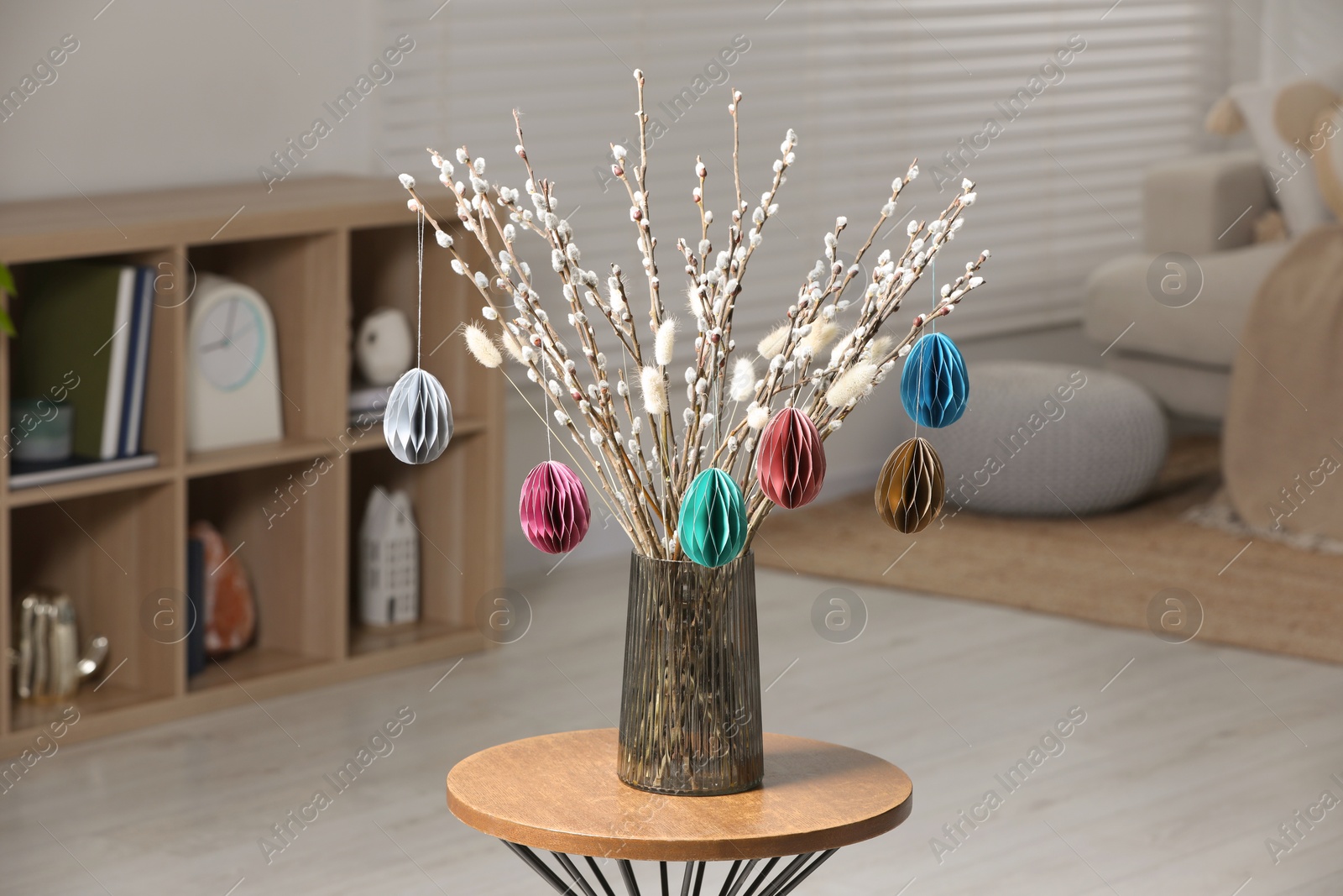 Photo of Beautiful pussy willow branches with paper eggs in vase on wooden table at home. Easter decor