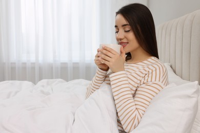 Photo of Beautiful young woman with cup of drink in bed at home