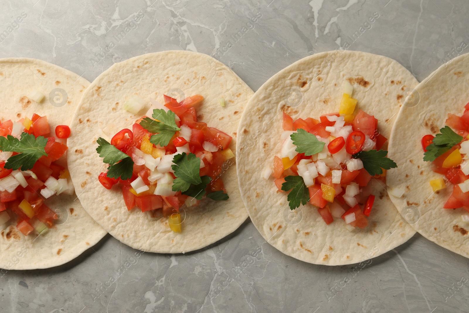 Photo of Delicious tacos with vegetables and parsley on grey marble table, top view