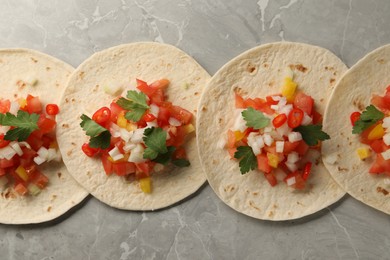 Delicious tacos with vegetables and parsley on grey marble table, top view